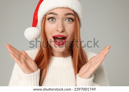 Emotional young woman in Santa hat on light grey background. Christmas celebration