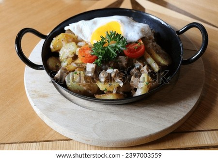 authentic tyrolean farmers dish using leftovers of meat, onion and potatoes topped with a sunny side up egg served in small skillet Royalty-Free Stock Photo #2397003559
