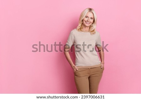 Photo of pleasant charming person with blond hairstyle dressed striped t-shirt keep hands in pockets isolated on pink color background