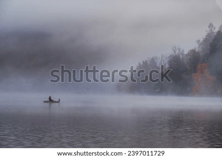 A lone fisherman in a small boat. Romantic foggy autumn morning on Lake Bled, Slovenia.