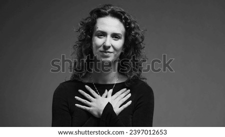 Heartfelt moment of woman putting hands on chest feeling thankful and sincere gratitude in black and white, monochrome Royalty-Free Stock Photo #2397012653