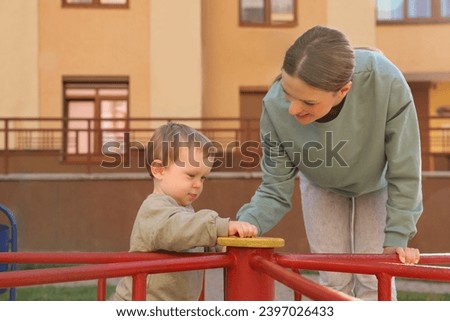 Happy nanny and cute little boy on carousel outdoors