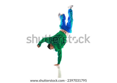 Fashionable portrait. Stylishly dressed man dancing in freestyle, breakdance style in motion against white studio background. Concept of action, sport, lifestyle, youth. Dancer shows breakdance figure
