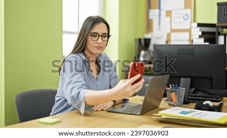Young beautiful hispanic woman business worker make selfie by smartphone at office