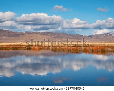 Beautiful autumn mountain lake and mountains. Reflection of snowy peaks and dry yellow grass in the steppe on the surface of a mountain lake. 
