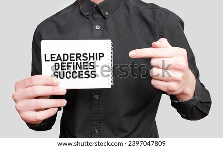 Businessman holding a white notepad with text LEADERSHIP DEFINES SUCCESS, business concept