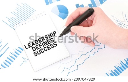 Businessman holding a black marker, notepad with text LEADERSHIP DEFINES SUCCESS, business concept