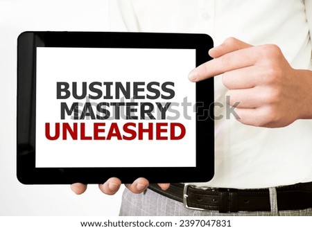 Text BUSINESS MASTERY UNLEASHED on tablet display in businessman hands on the white background. Business concept