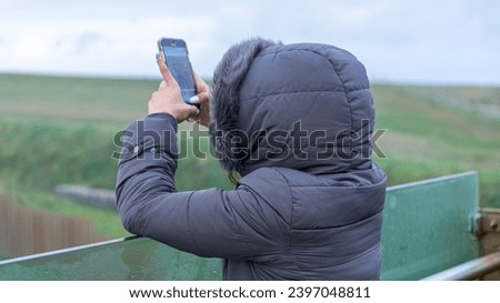 Woman taking photos with her hooded phone on a very cold day.