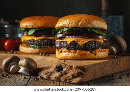 Two delicious homemade burgers of beef, cheese and mushrooms on an old wooden table. Fat unhealthy food close-up.