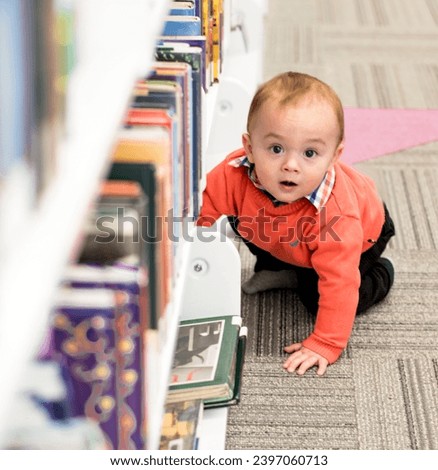 A bright-eyed baby, dressed in a vibrant orange sweater and checkered collar, is captured in a moment of discovery, reaching out towards the colorful bookshelves in a library.