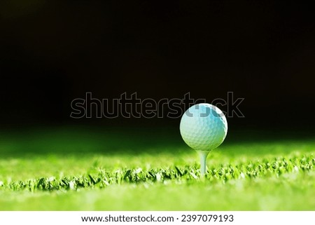 Close-up of white golf ball on tee with blur green and black bokeh background. Golf game concept