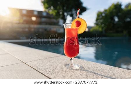 refreshing red cocktail garnished with a strawberry and orange slice by a poolside at sunset