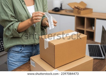 A woman customer labels a cardboard parcel with a barcode for a swift online shopping refund.  Royalty-Free Stock Photo #2397084473