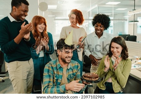 An inclusive diverse businesspeople are clapping and singing a birthday song to a man with bday cake in hands while celebrating at workspace. A businesspeople making a having a surprise bday party.
