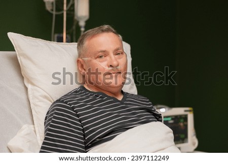 Portrait of hospitalized senior gentleman, with an oxygen tube in his nose and fingertip oxygen monitor, resting in bed. Royalty-Free Stock Photo #2397112249