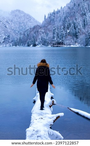 Winter landscape A girl walks along a snow-covered lake Rear view against the backdrop of a mountain in the snow and a forest A winter's tale Abkhazia Lake Rizza Winter atmosphere New Year's forest Wa