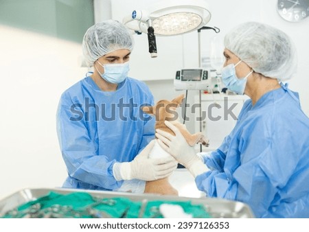Focused young veterinarian with elderly female assistant, examining cute little Chihuahua with bandaged abdomen after surgical operation in veterinary clinic operating room