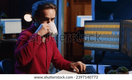 Photographer using software on computer to perform editing operations, enjoying cup of coffee while correcting images. Photo editor using PC to make adjustments to photographs in studio