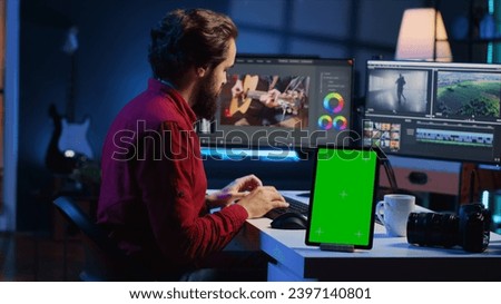Video editor adds sound effects to filmed footage, working in post production studio with green screen tablet. Videographer using headphones to test and improve audio quality next to mockup device