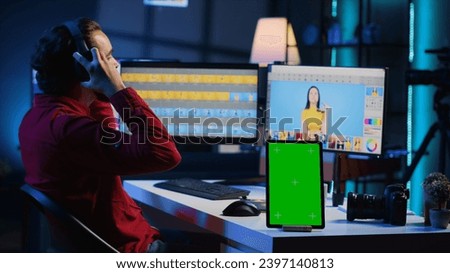 Chroma key tablet on desk next to photo editor working in independent production company. Isolated screen device and photographer adjusting white balance on overexposed pictures