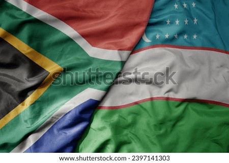 big waving national colorful flag of uzbekistan and national flag of south africa . macro