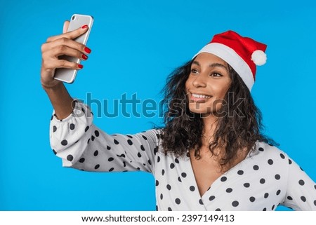Young african american woman wearing Christmas hat and taking selfie on smartphone over isolated background. New Year celebration. Social media posting, vlogging and blogging