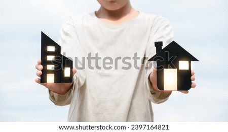 Man hands holding miniature black house and commercial building model with soft light in sky background for concept of home insurance and real estate.