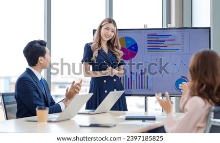 Asian professional successful female businesswoman presenter lecturer speaker in formal business outfit stand hold pen pointing presenting graph chart strategy data on computer screen in meeting room.