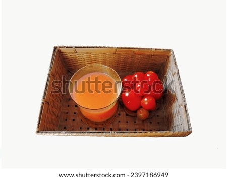 In the picture, there is a rectangular brown bamboo woven basket. Inside, there are some red-orange tomatoes and a glass of orange tomato juice placed nearby.