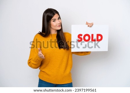 Young Brazilian woman isolated on white background holding a placard with text SOLD making a deal