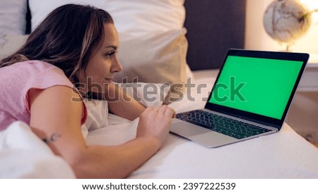 Young woman lies on the bed with her laptop - green screen display - home shooting