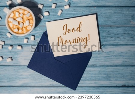 GOOD MORNING text on valentine card inscription positive quote phrase Greeting card blue envelope with white cup of coffee and marshmallows on wooden blue background holiday
