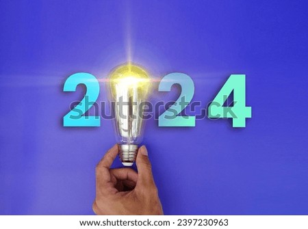 Happy New Year 2024 greeting card with light bulbs. Glowing 2024 calendar, creative trend light bulb held by businessman hand shining luminously. 