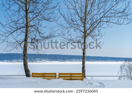 Capture the beauty of winter in a photo A sunny day illuminates a bright yellow park bench A river covered in ice and snow creates a serene atmosphere