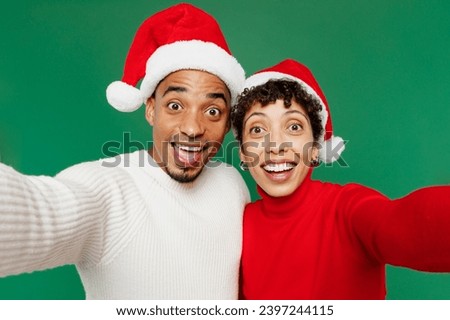 Close up merry young couple man woman wear red casual clothes Santa hat posing do selfie shot pov on mobile cell phone isolated on plain green background. Happy New Year 2024 Christmas holiday concept