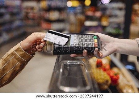 Close up cropped photo customer holding wireless bank payment terminal process acquire credit card shopping at supermaket store grocery shop buying products inside hypermarket. Purchasing food concept