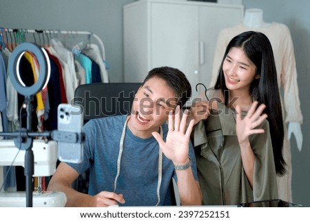 Happy Asian designers in design studio making a live steaming video on social network together, designer showing their works on social network live steaming. Couple selling clothes on social media.