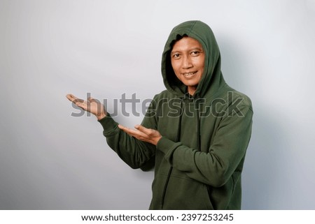 Attractive Asian man wearing green hoodie pointing fingers beside