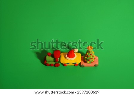 A toy train with a Christmas tree and a Santa Claus hat made of plasticine. Green background.