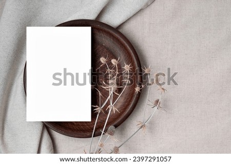 Minimalist aesthetic wedding design or business brand template, empty paper card mockup on brown plate with dried meadow flowers, on neutral beige linen fabric, earthy sustainable backdrop.
