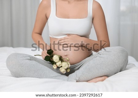 Pregnant woman with roses sitting on bed indoors, closeup