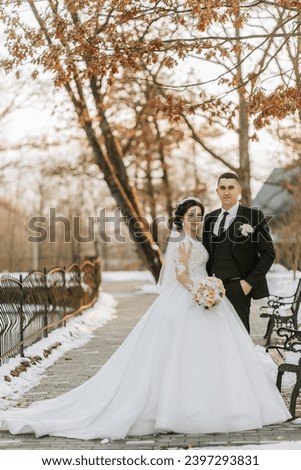 Winter wedding. Happy couple walking in wedding clothes hugging and smiling in a winter park covered with snow on their wedding day. Winter love story of a beautiful couple in snowy winter weather