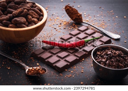 Dark chocolate bar, red hot chilli pepper cayenne,  dry hot chili spices, cocoa beans nibs powder, food tasty design on black wooden background