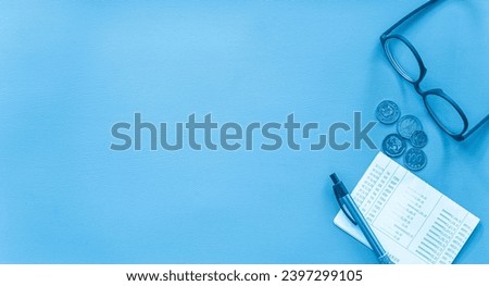 Flat lay view of money coin, eyeglasses, pen and book bank on blue leather background with copy space. Business and financial concept.  Royalty-Free Stock Photo #2397299105