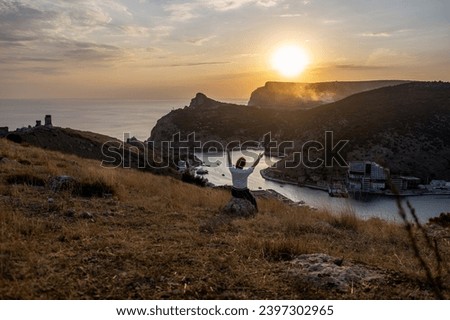 Happy woman on sunset in mountains. Woman siting with her back on the sunset in nature in summer with open hands. Silhouette.
