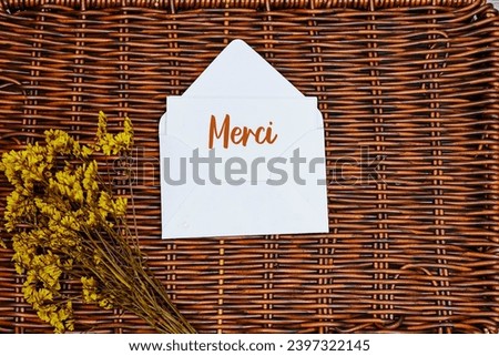 Merci french word mean thank you in english  card in an envelope with yellow gypsophila flower on esparto halfah background
