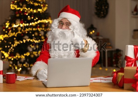 Santa Claus showing thumb up while signing Christmas letters at home Royalty-Free Stock Photo #2397324307