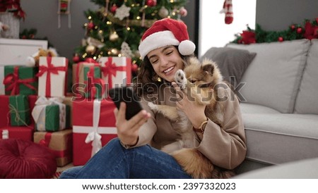 Young hispanic woman with dog make selfie by smartphone celebrating christmas at home