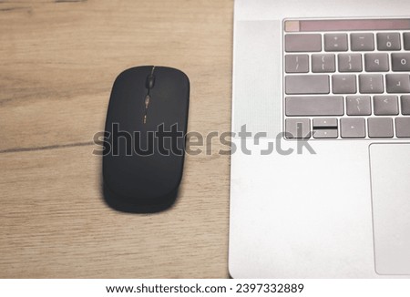 Black wireless minimalist mouse near the gray laptop . Modern technology device.